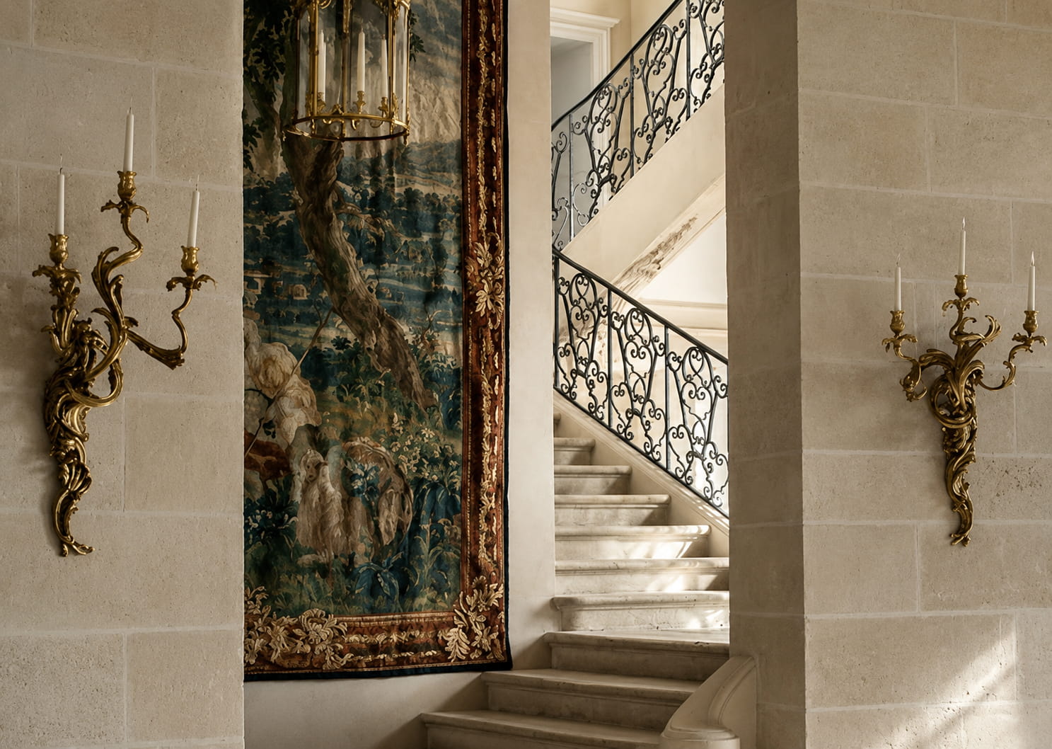 A château interior with stone staircase, antique tapestry, and gilt sconces